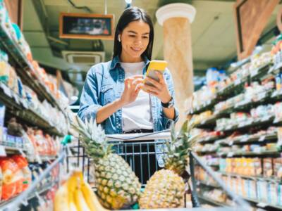 ragazza che fa la spesa con lo smartphone in mano e l'ananas nel carrello