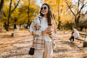 donna con look autunnale al parco che beve un caffe