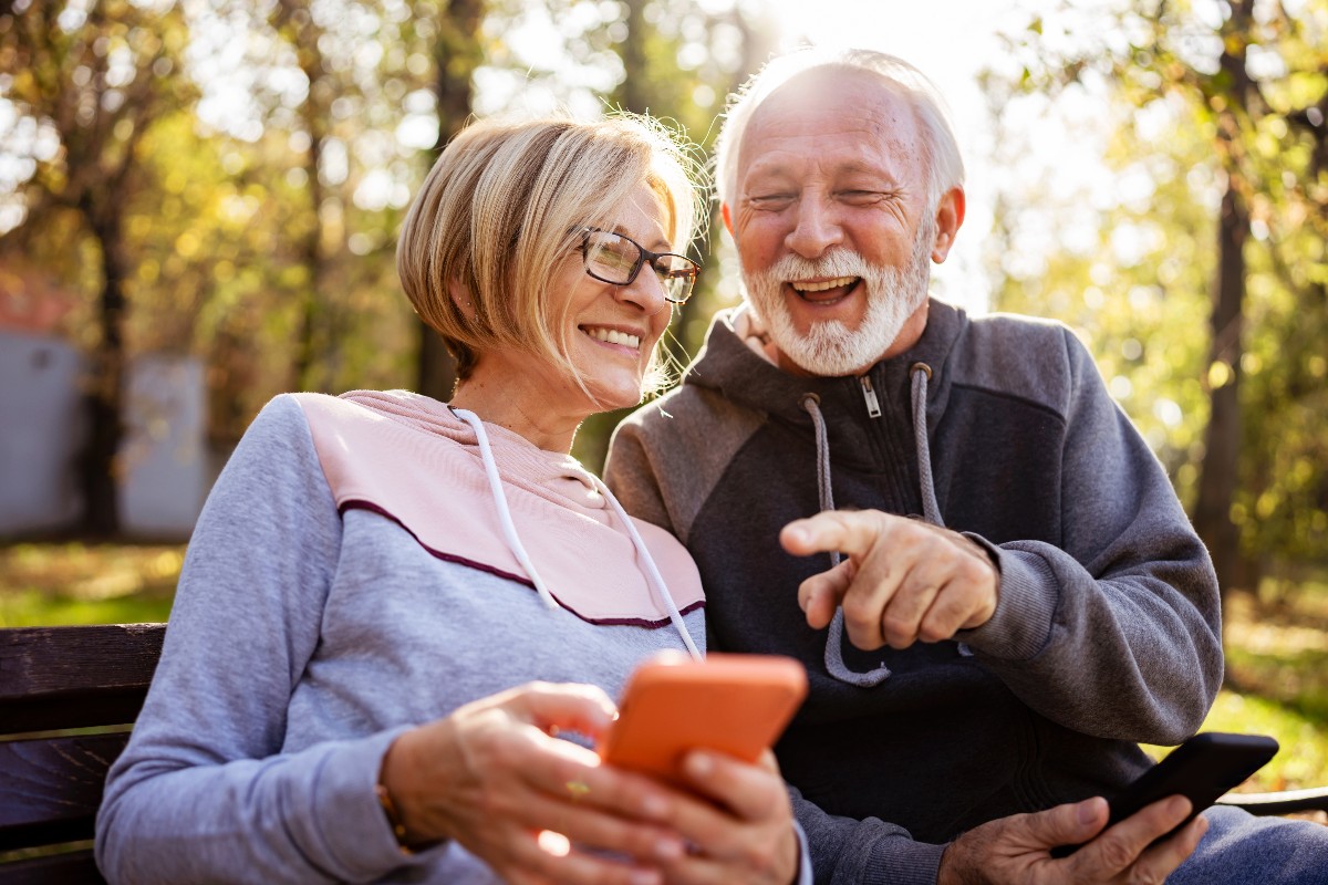 anziani seduti su una panchina che ridono guardando lo smartphone