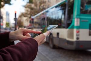 persona con smartphone fermo in citta con autobus che passa