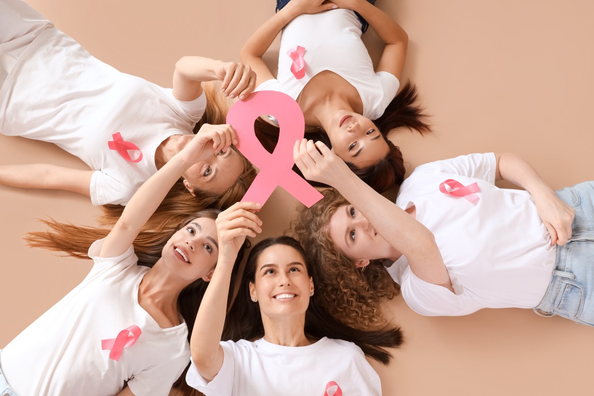 Donne sorridenti che tengono in mano il fiocco rosa simbolo della lotta contro il cancro